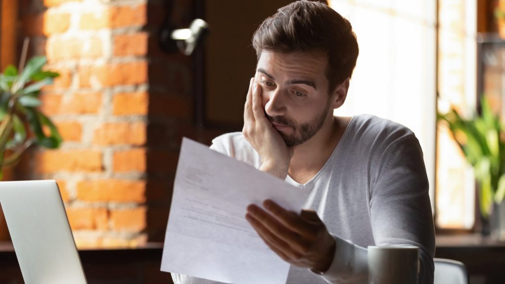 Confused,Frustrated,Young,Man,Reading,Letter,In,Cafe,,Debt,Notification,